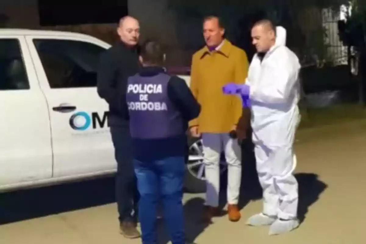 Cuatro personas conversan junto a una camioneta blanca, una de ellas lleva un chaleco de la policía de Córdoba y otra viste un traje de protección blanco Cuatro personas conversan junto a una camioneta blanca, una de ellas lleva un chaleco de la policía de Córdoba y otra viste un traje de protección blanco