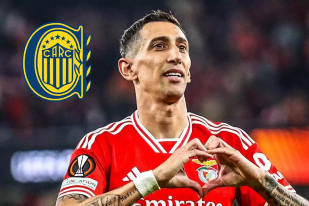 Futbolista con uniforme rojo celebrando con las manos en forma de corazón y el escudo de Rosario Central al fondo