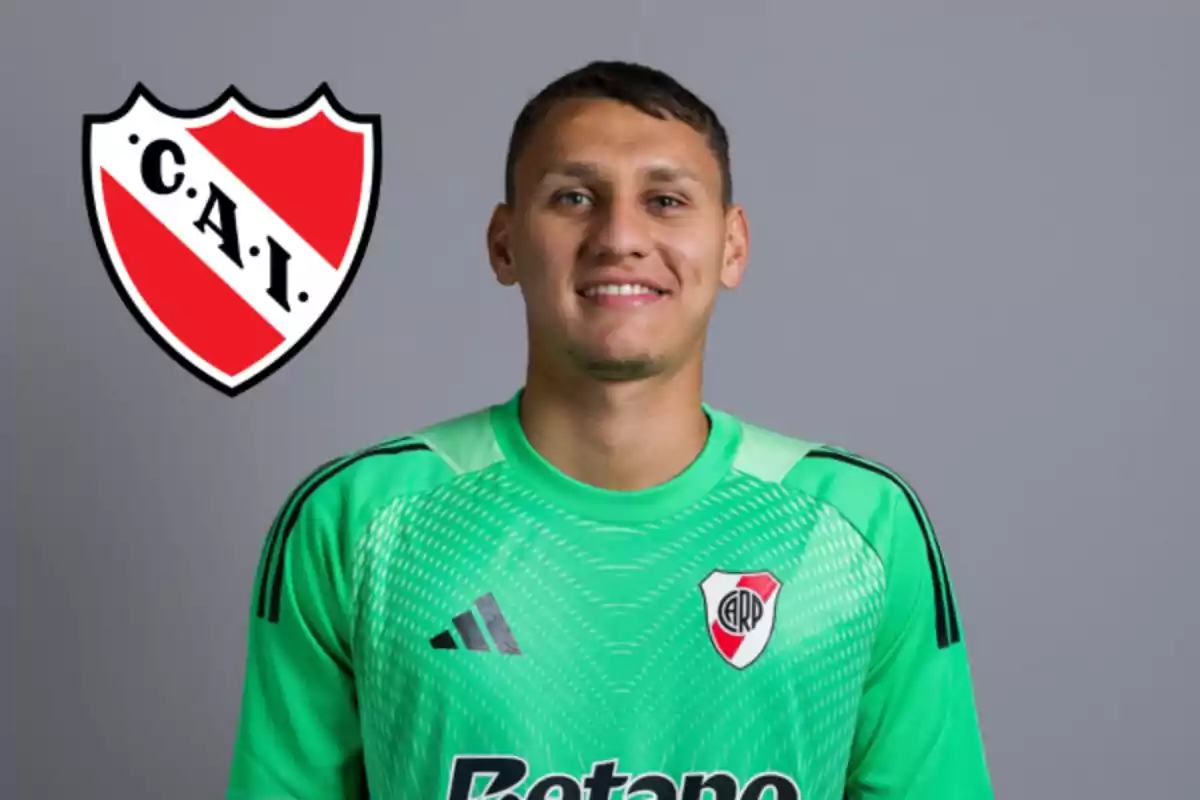 Portero con camiseta verde de River Plate sonriendo frente a un fondo gris y el escudo de Independiente a la izquierda