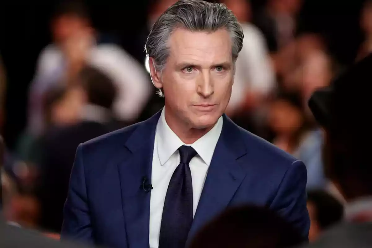 Hombre de cabello canoso con traje azul y corbata oscura en un evento con personas desenfocadas al fondo Hombre de cabello canoso con traje azul y corbata oscura en un evento con personas desenfocadas al fondo
