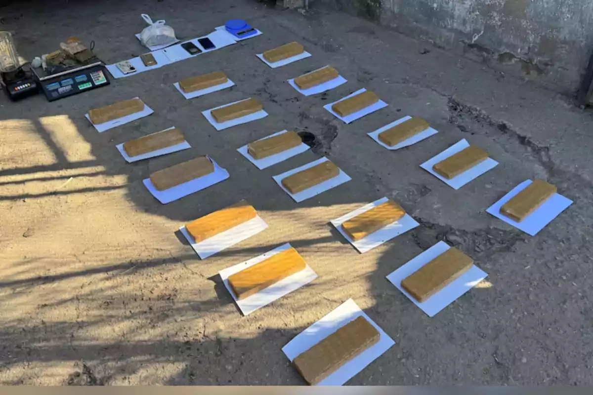 Paquetes envueltos en cinta color marrón organizados sobre hojas blancas en el suelo junto a básculas, licuadora, teléfonos y otros objetos Paquetes envueltos en cinta color marrón organizados sobre hojas blancas en el suelo junto a básculas, licuadora, teléfonos y otros objetos