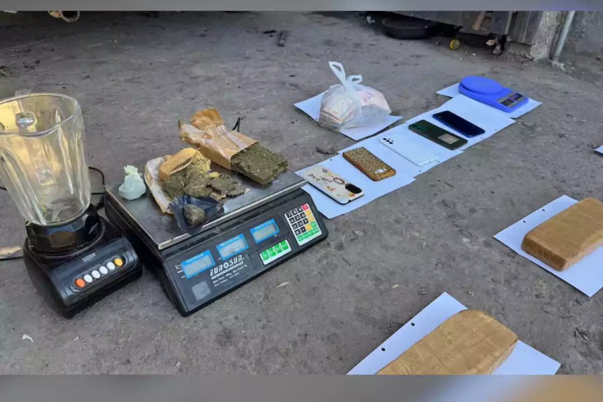 Objetos incautados sobre el suelo incluyendo una licuadora, una báscula digital, varios paquetes envueltos, teléfonos móviles y una bolsa de plástico con billetes Objetos incautados sobre el suelo incluyendo una licuadora, una báscula digital, varios paquetes envueltos, teléfonos móviles y una bolsa de plástico con billetes