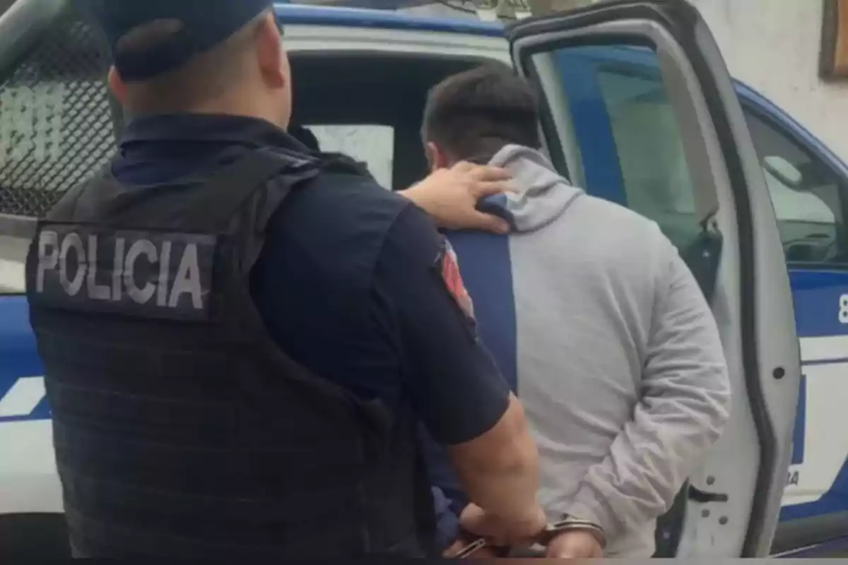 Un policía escolta a un hombre esposado hacia una patrulla policial