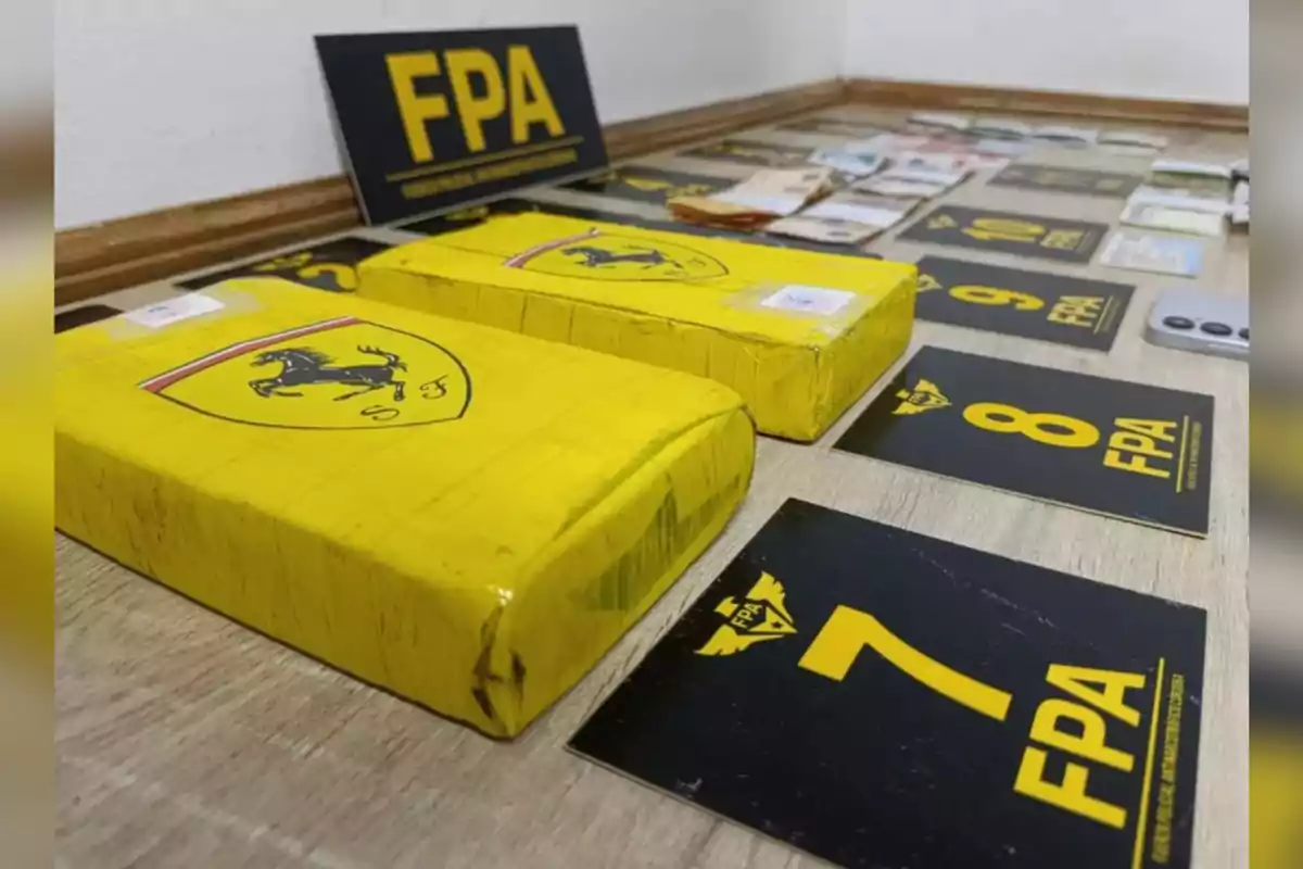 Paquetes rectangulares envueltos en cinta amarilla con el logo de Ferrari junto a tarjetas numeradas y billetes sobre una mesa
