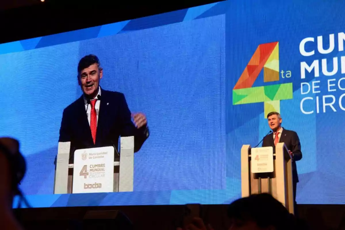 Un hombre con traje y corbata roja da un discurso en un podio durante la 4ta Cumbre Mundial de Economía Circular en Córdoba mientras es proyectado en una pantalla gigante detrás de él
