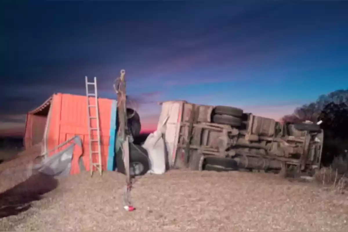 Camión de carga volcado sobre su costado en un camino de tierra al atardecer con una escalera apoyada en la caja del vehículo Camión de carga volcado sobre su costado en un camino de tierra al atardecer con una escalera apoyada en la caja del vehículo