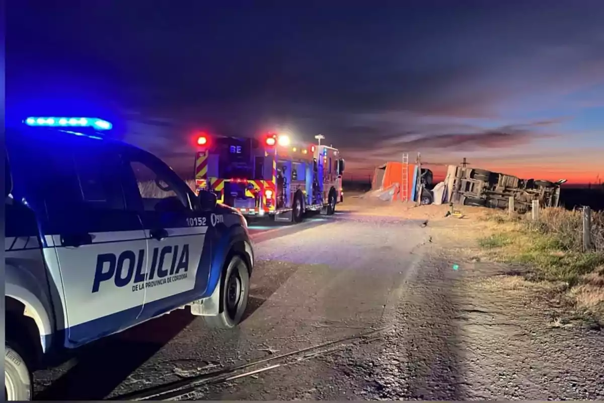 Patrulla de policía y camión de bomberos atendiendo un accidente de un camión volcado al costado de una carretera al atardecer Patrulla de policía y camión de bomberos atendiendo un accidente de un camión volcado al costado de una carretera al atardecer