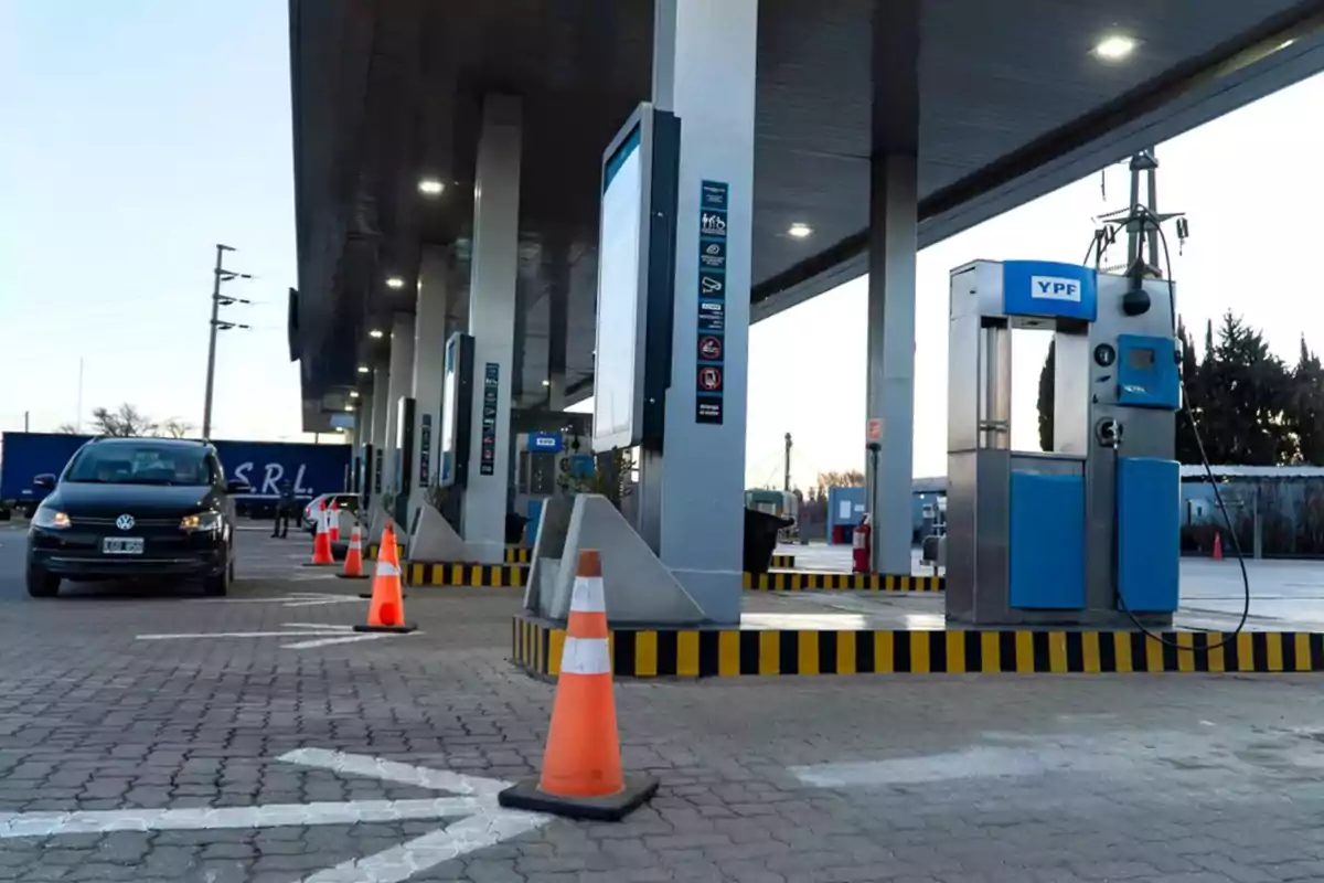 Gas station with fuel pumps and orange cones marking the area as a black car approaches Gas station with fuel pumps and orange cones marking the area as a black car approaches