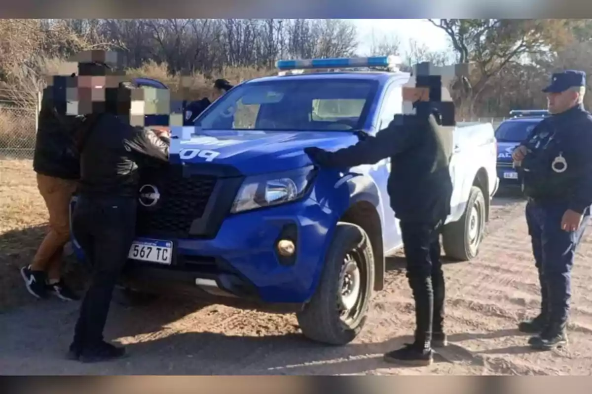 Several people are being checked by the police next to a blue patrol car on a dirt road. Several people are being checked by the police next to a blue patrol car on a dirt road.
