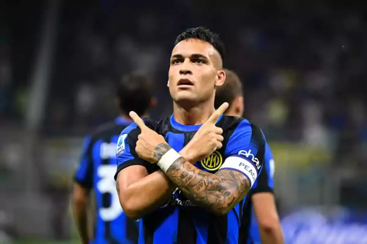 Futbolista con uniforme azul y negro celebrando un gol con los brazos cruzados y los dedos señalando hacia arriba Futbolista con uniforme azul y negro celebrando un gol con los brazos cruzados y los dedos señalando hacia arriba