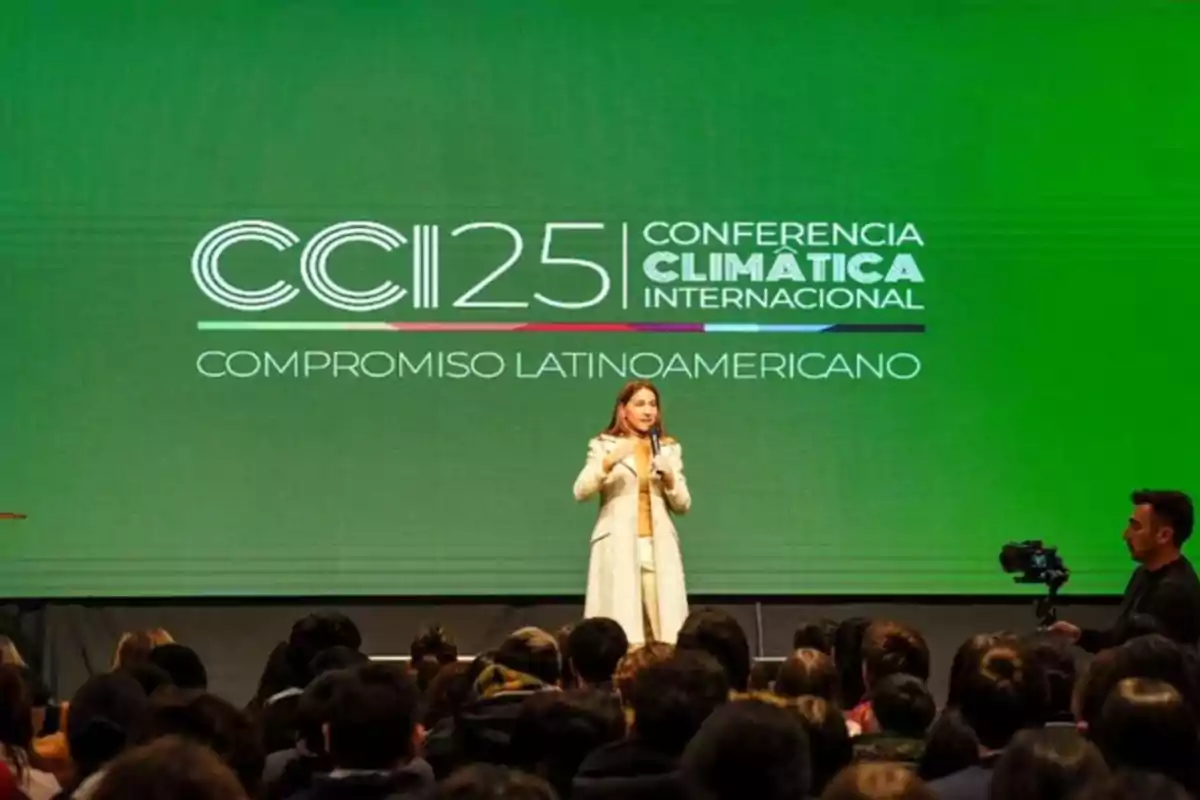 Woman speaking on a stage in front of an audience with a green screen in the background displaying the text CCI25 International Climate Conference Latin American Commitment Woman speaking on a stage in front of an audience with a green screen in the background displaying the text CCI25 International Climate Conference Latin American Commitment