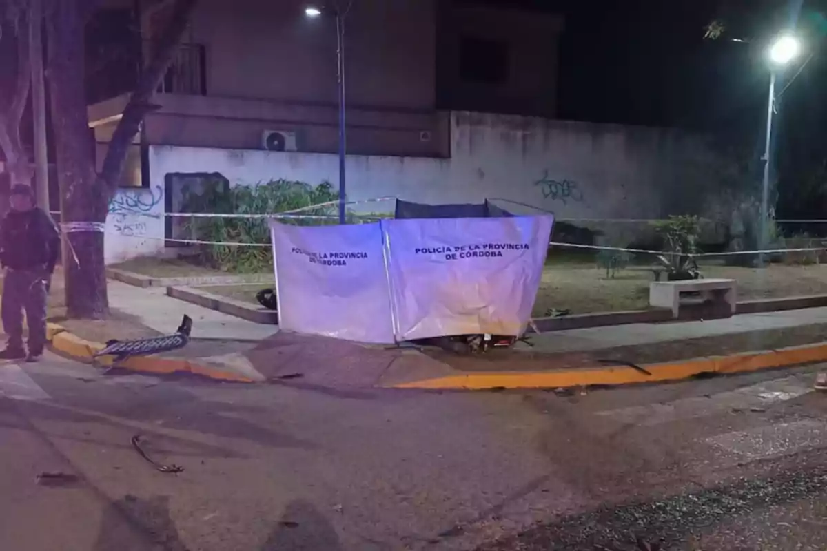 Nighttime scene of a traffic accident at a corner cordoned off by Córdoba police, with a canopy covering part of the sidewalk and vehicle debris on the ground. Nighttime scene of a traffic accident at a corner cordoned off by Córdoba police, with a canopy covering part of the sidewalk and vehicle debris on the ground.