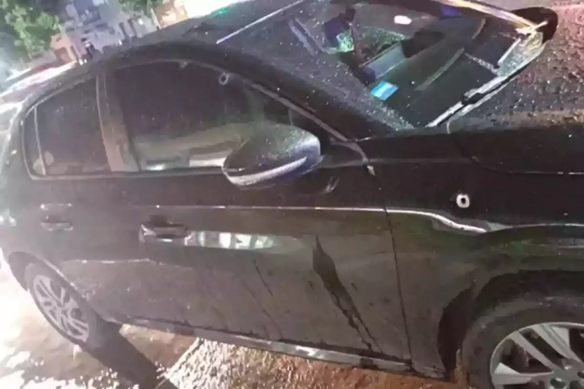 Auto negro con impactos de bala en la puerta y la ventana rota bajo la lluvia en una calle urbana Auto negro con impactos de bala en la puerta y la ventana rota bajo la lluvia en una calle urbana