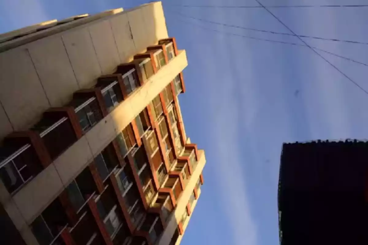 Tall building seen from below with blue sky and some electric wires crossing at the top Tall building seen from below with blue sky and some electric wires crossing at the top