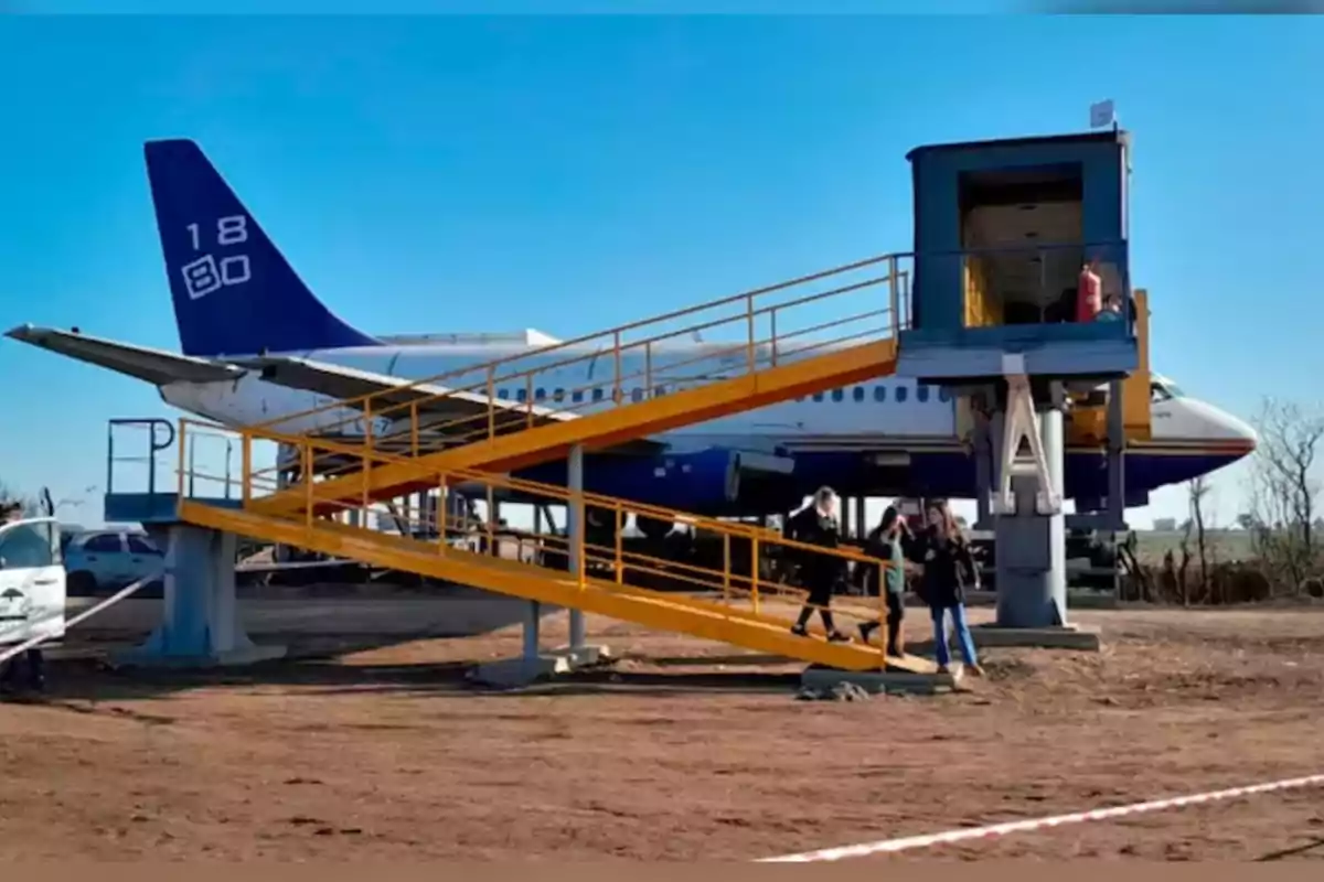 Plane adapted as a building with a yellow ramp and people descending in an outdoor setting Plane adapted as a building with a yellow ramp and people descending in an outdoor setting