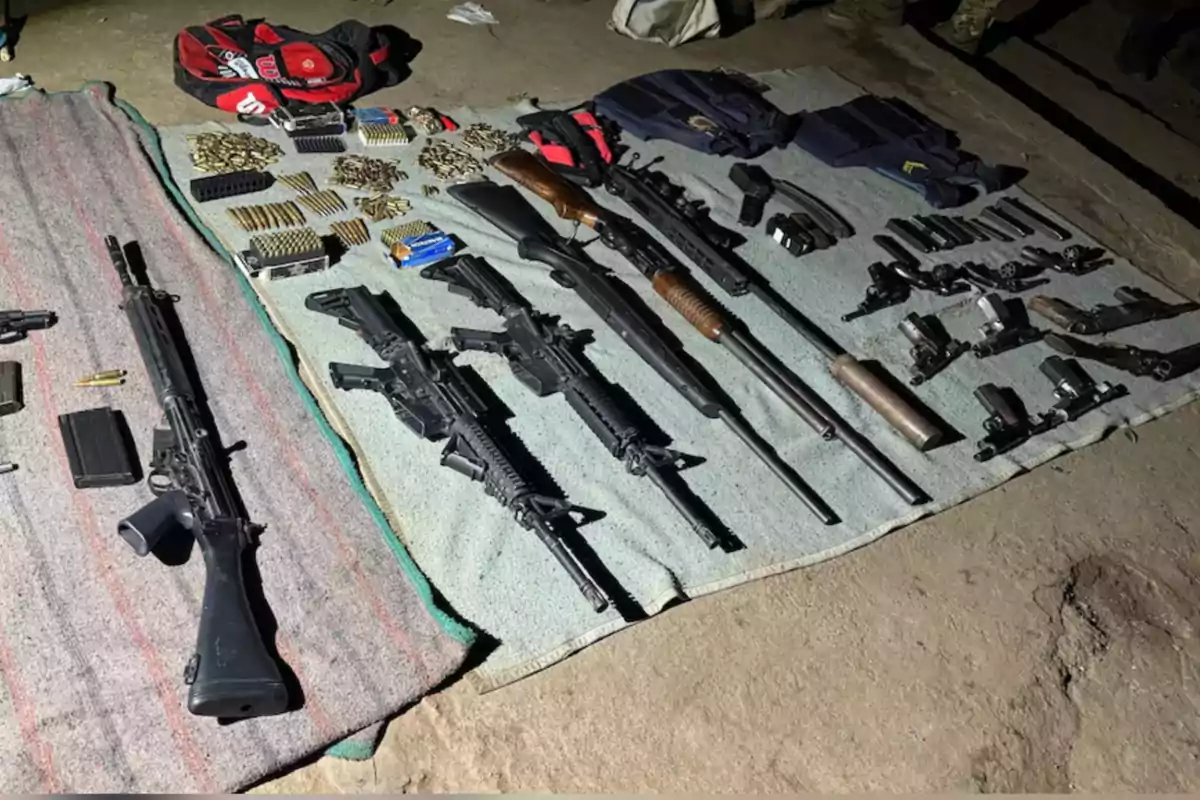 Long and short firearms, ammunition, magazines, and bulletproof vests arranged on blankets on the ground