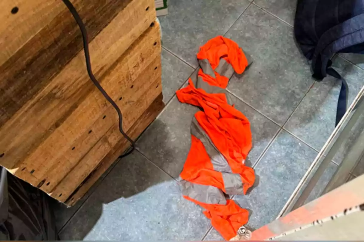 Orange safety vest with reflective stripes lying on the ground next to a wooden pallet and a blue backpack Orange safety vest with reflective stripes lying on the ground next to a wooden pallet and a blue backpack