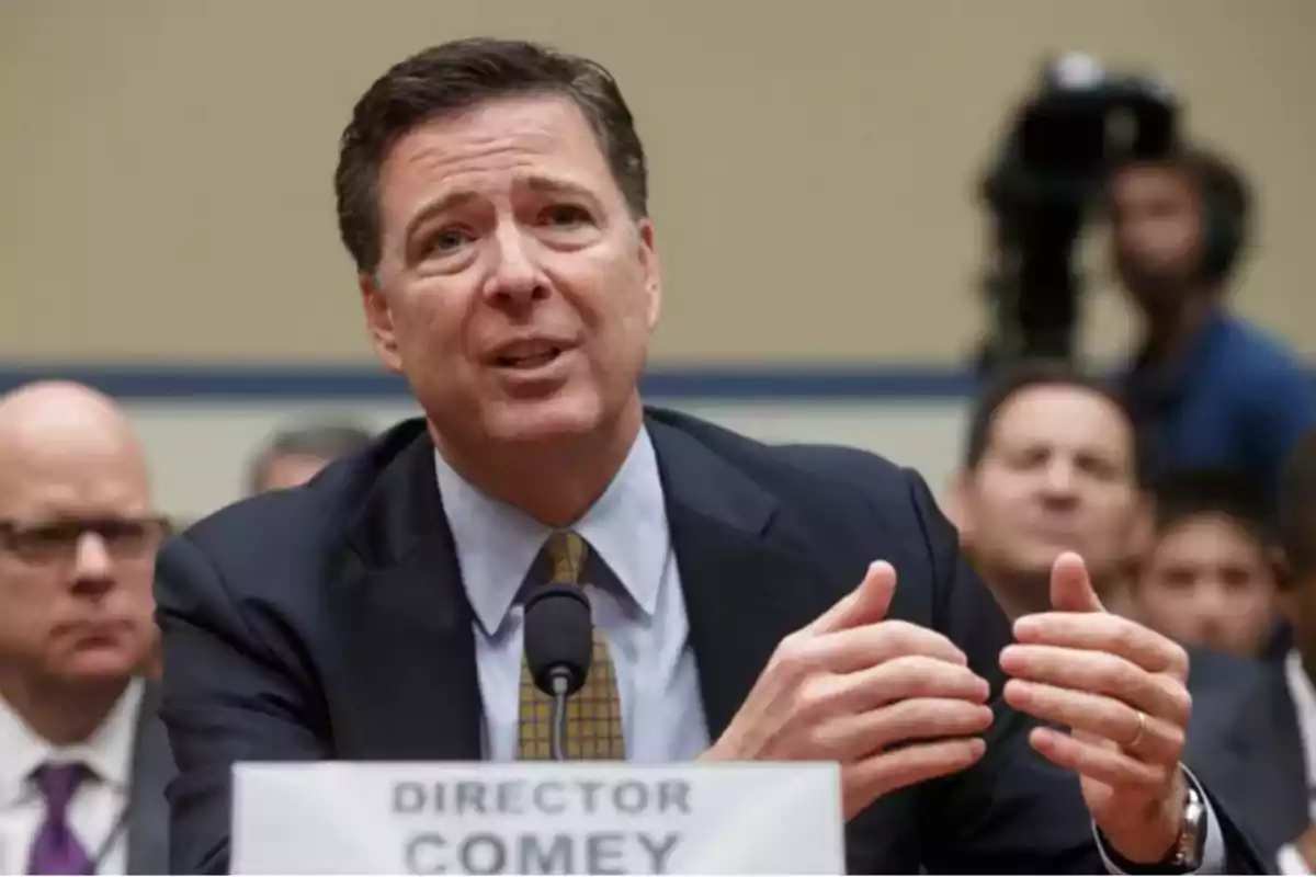 Man in a suit speaking into a microphone at a public hearing with people in the background