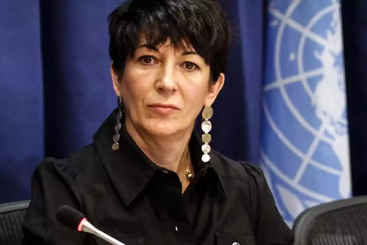 Mujer de cabello corto y oscuro con pendientes largos sentada frente a un micrófono con una bandera de la ONU de fondo Mujer de cabello corto y oscuro con pendientes largos sentada frente a un micrófono con una bandera de la ONU de fondo