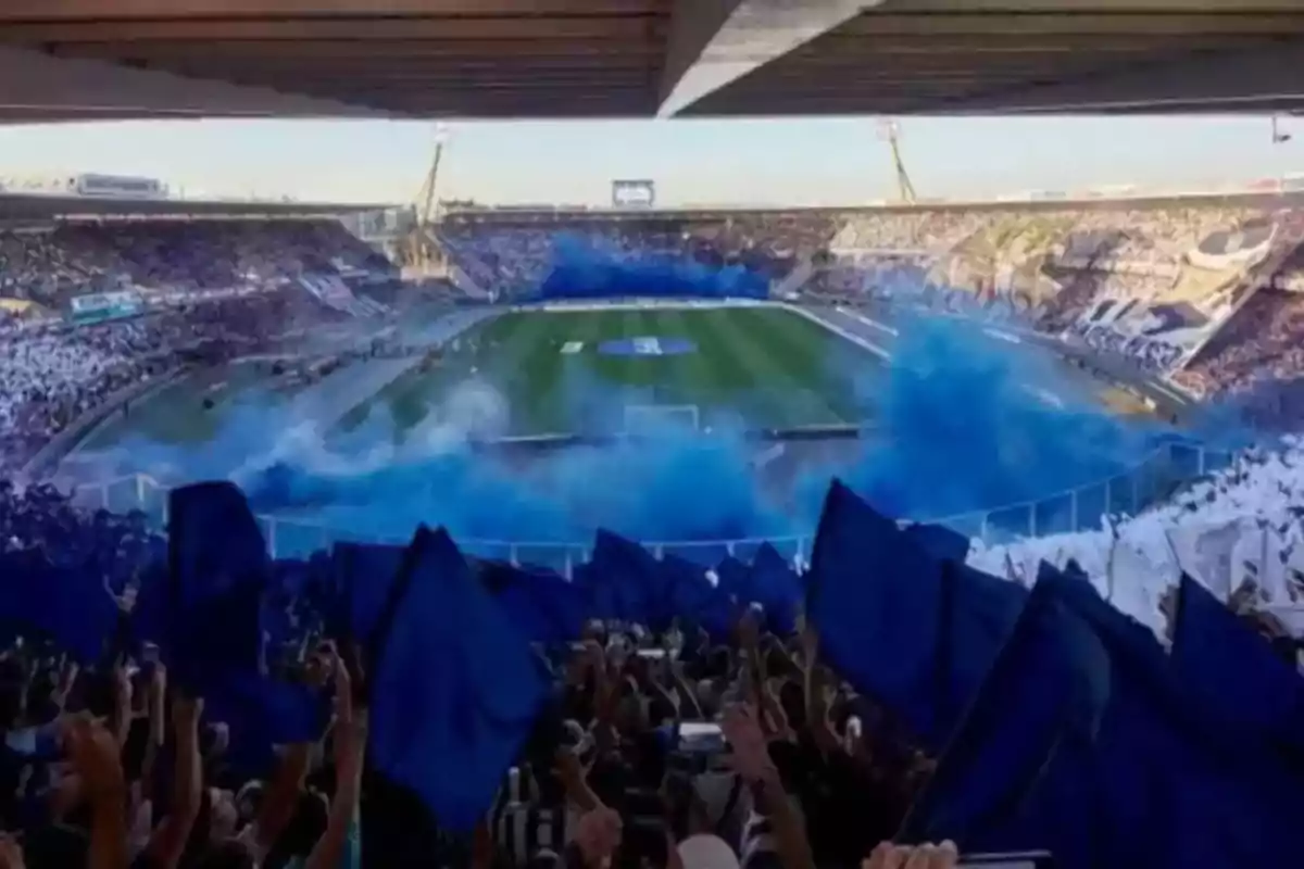 Fans cheering in a soccer stadium with blue flags and smoke of the same color filling the air during an important match Fans cheering in a soccer stadium with blue flags and smoke of the same color filling the air during an important match