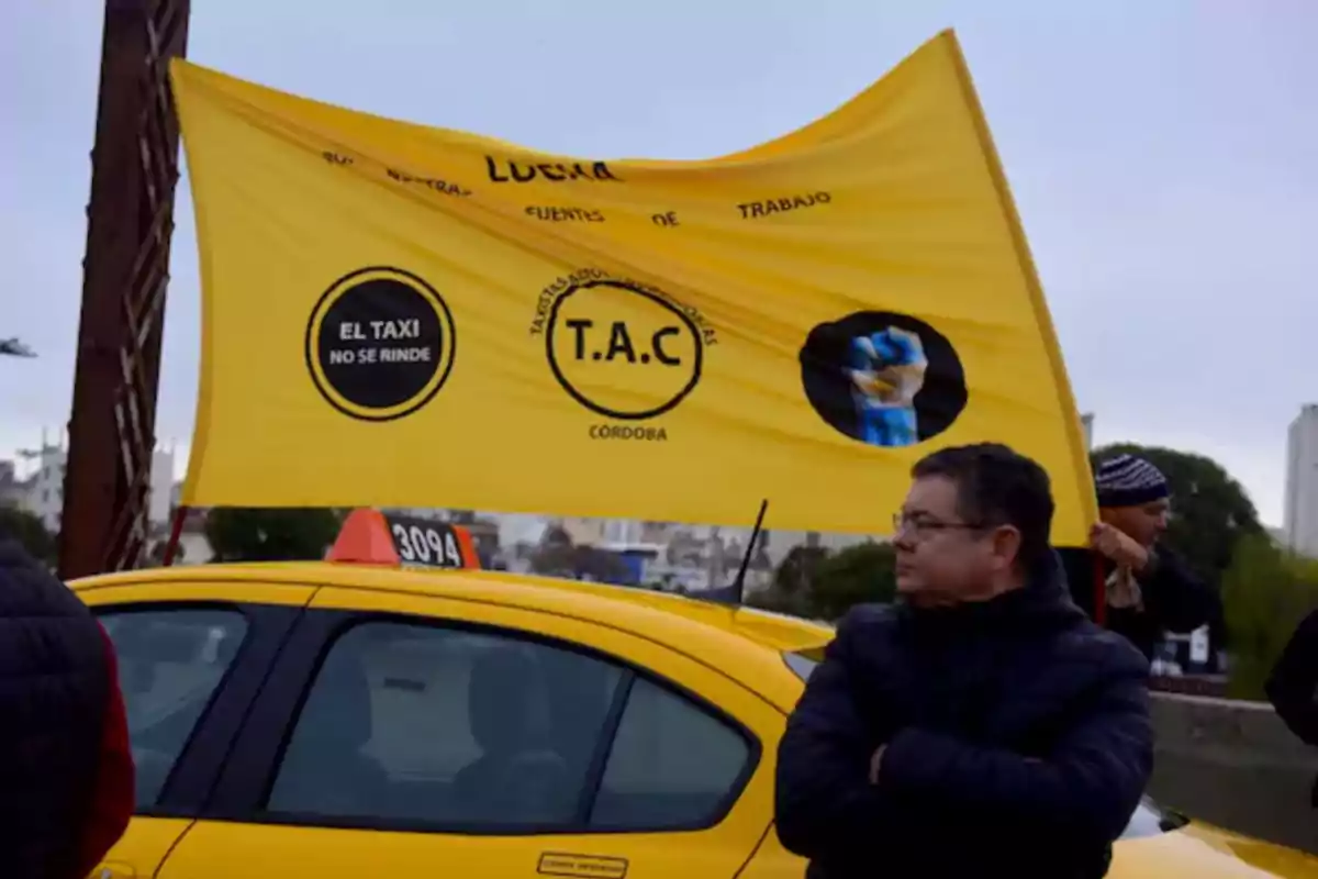 Hombre de pie junto a un taxi amarillo con una bandera amarilla que tiene mensajes de apoyo a los taxistas en Córdoba Hombre de pie junto a un taxi amarillo con una bandera amarilla que tiene mensajes de apoyo a los taxistas en Córdoba
