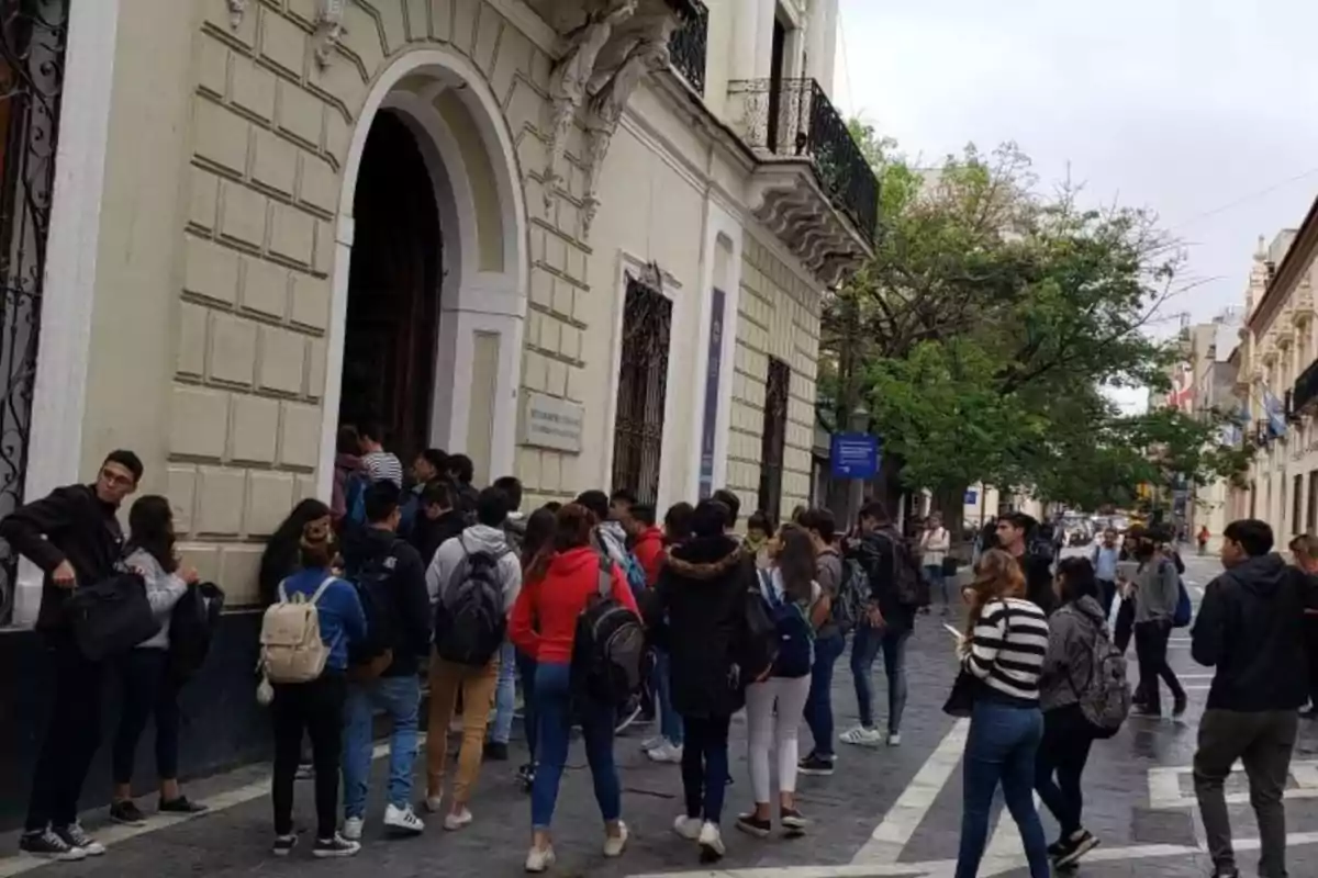 Grupo de jóvenes con mochilas esperando para entrar a un edificio antiguo en una calle urbana Grupo de jóvenes con mochilas esperando para entrar a un edificio antiguo en una calle urbana