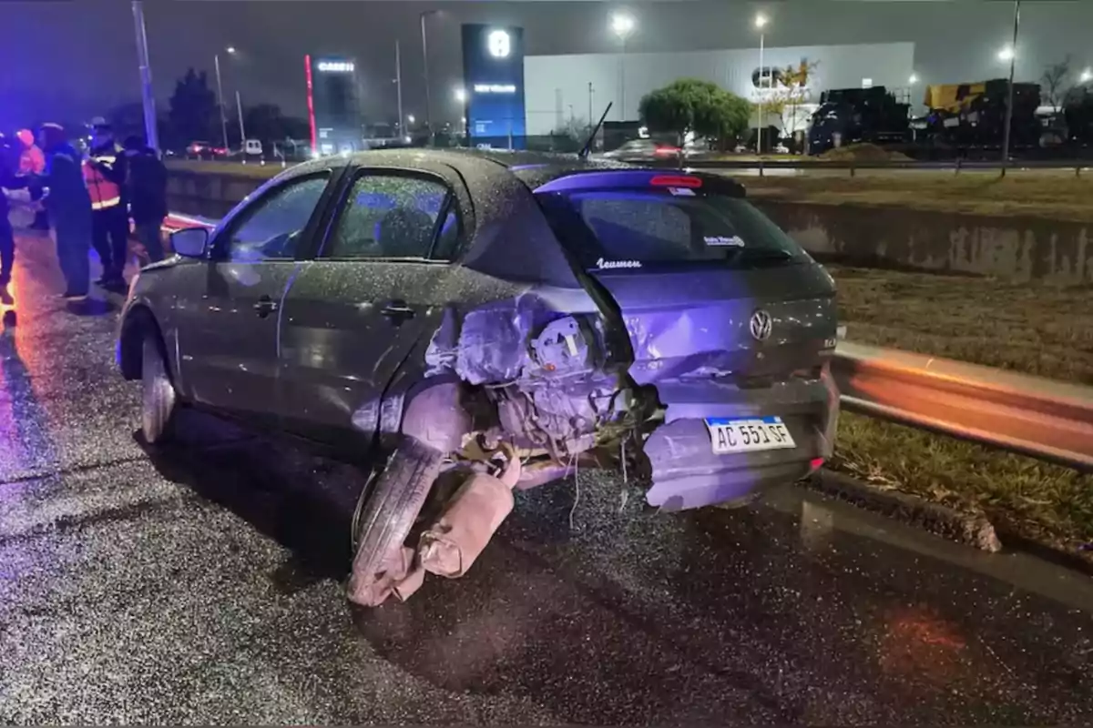 Gray car with severe rear damage after an accident on a wet road at night, with emergency lights and several people in the background Gray car with severe rear damage after an accident on a wet road at night, with emergency lights and several people in the background