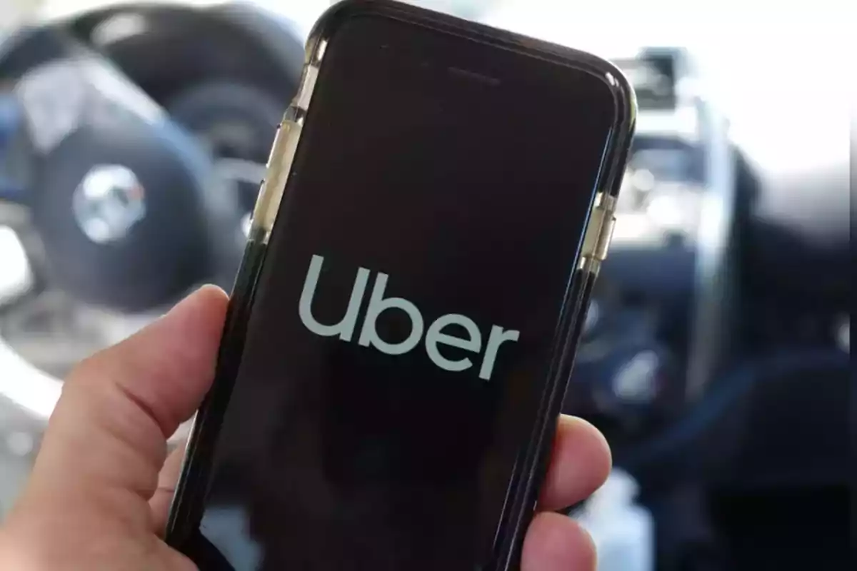 Persona sosteniendo un teléfono móvil con la pantalla mostrando el logo de Uber dentro de un automóvil Persona sosteniendo un teléfono móvil con la pantalla mostrando el logo de Uber dentro de un automóvil