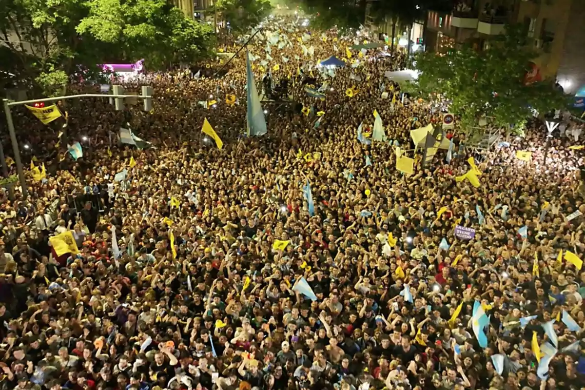 Crowd of people gathered at a nighttime demonstration in the street, many of them holding flags and banners under the light of street lamps and surrounded by trees. Crowd of people gathered at a nighttime demonstration in the street, many of them holding flags and banners under the light of street lamps and surrounded by trees.
