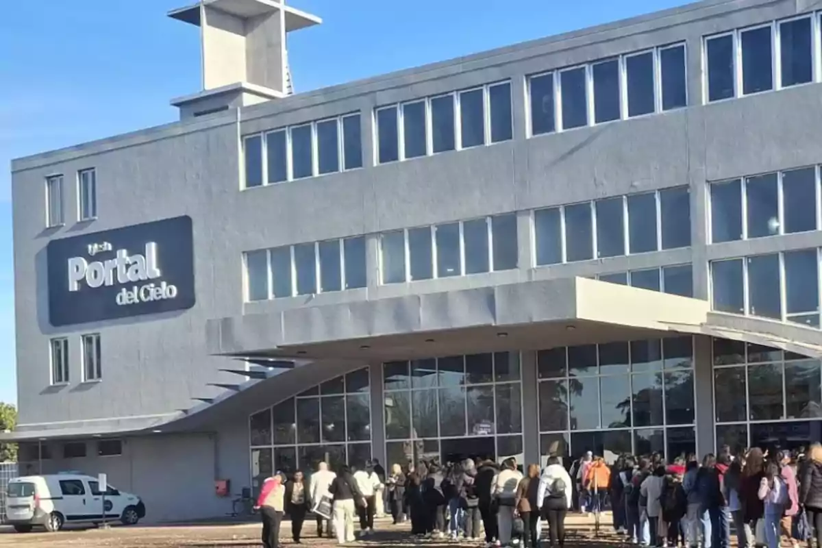 Un grupo de personas hace fila para ingresar a un edificio gris de varios pisos con grandes ventanales y un cartel que dice Portal del Cielo. Un grupo de personas hace fila para ingresar a un edificio gris de varios pisos con grandes ventanales y un cartel que dice Portal del Cielo.