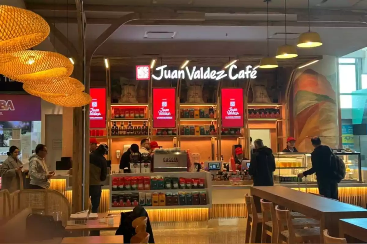 Cafetería Juan Valdez Café con varias personas haciendo fila y empleados atendiendo detrás del mostrador en un ambiente moderno y bien iluminado