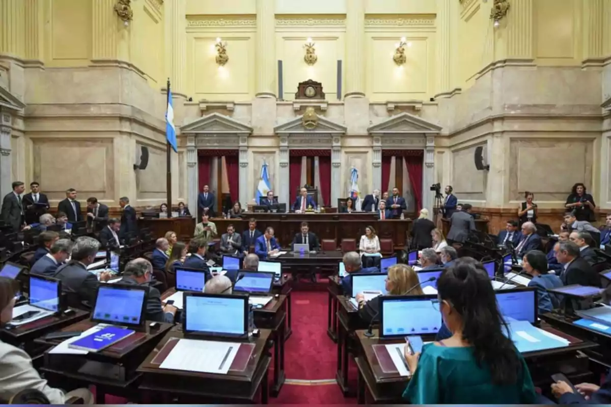 Sesión parlamentaria en el Senado de Argentina con legisladores sentados en sus bancas usando computadoras y banderas argentinas al fondo
