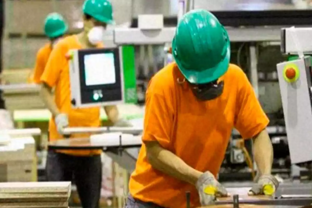 Trabajadores con casco y mascarilla operando maquinaria en una fábrica Trabajadores con casco y mascarilla operando maquinaria en una fábrica