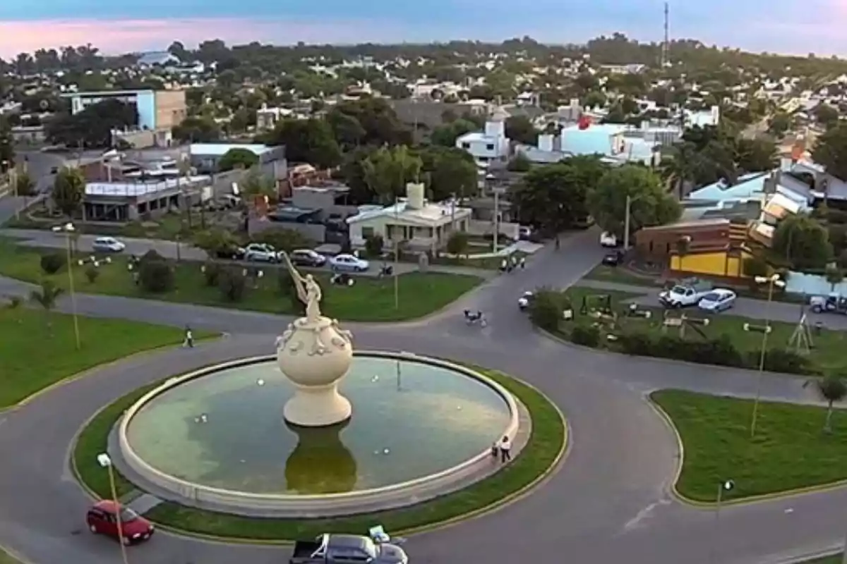 Vista aérea de una rotonda con una fuente central y una estatua, rodeada de calles, autos y casas en un barrio residencial Vista aérea de una rotonda con una fuente central y una estatua, rodeada de calles, autos y casas en un barrio residencial
