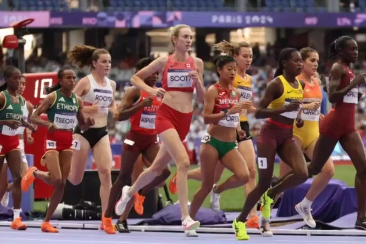 Varias atletas de diferentes países compiten en una carrera de pista durante un evento internacional de atletismo en un estadio.