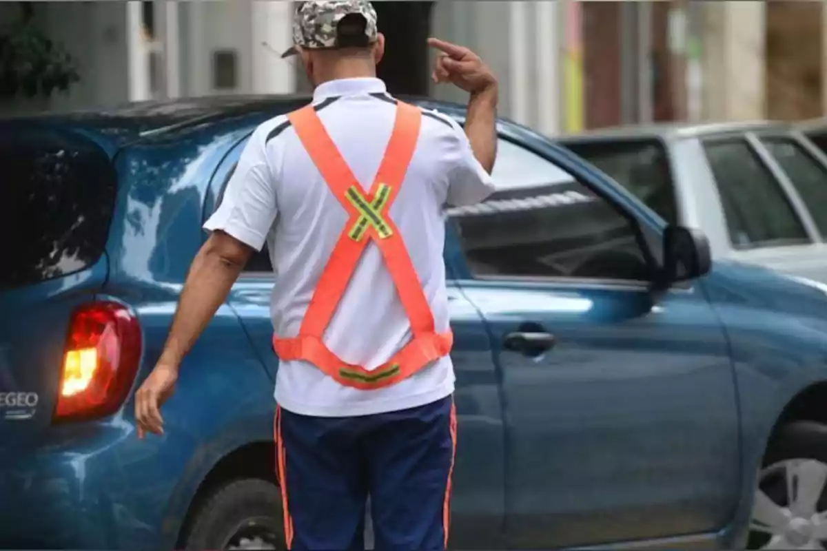 Man wearing an orange reflective vest directing a blue car where to park on the street Man wearing an orange reflective vest directing a blue car where to park on the street