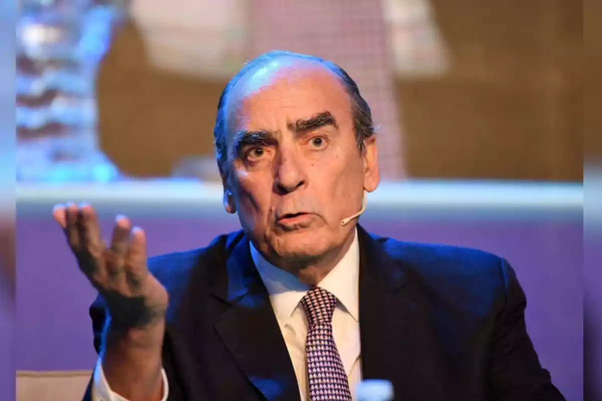 Man in a suit and tie speaking at an event with a microphone on his cheek and an expressive gesture with his raised hand Man in a suit and tie speaking at an event with a microphone on his cheek and an expressive gesture with his raised hand