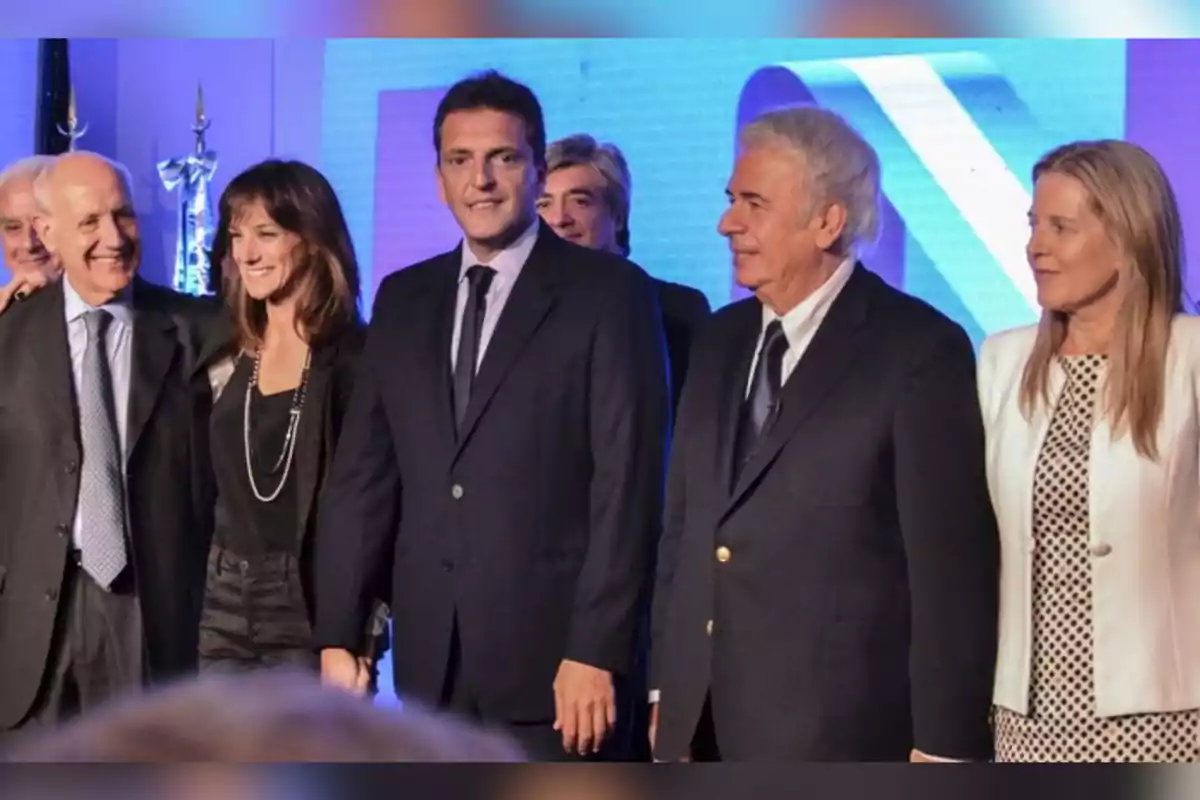 Group of people dressed formally posing together and smiling at an event with a blue background Group of people dressed formally posing together and smiling at an event with a blue background