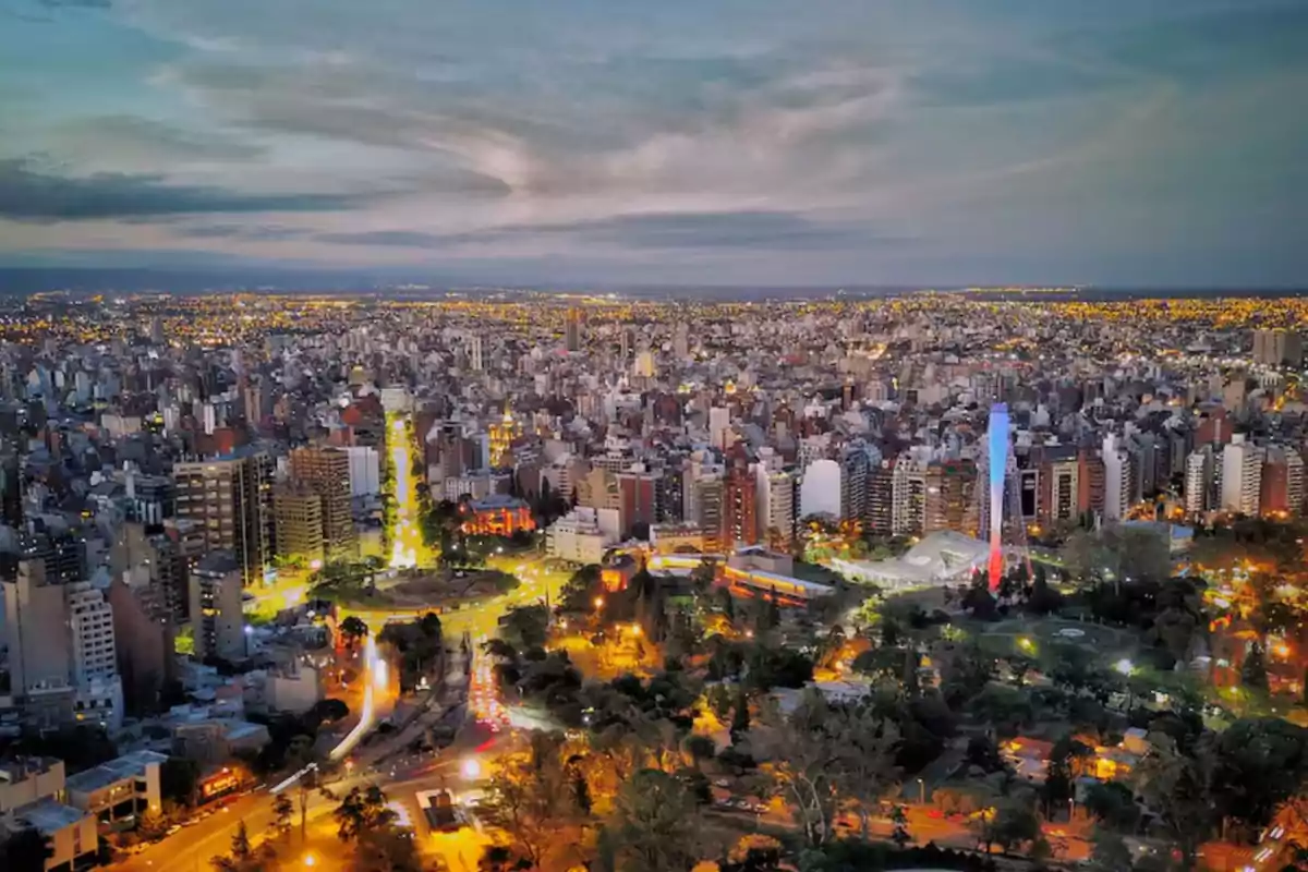Vista panorámica de una ciudad iluminada al anochecer con edificios altos, avenidas y áreas verdes