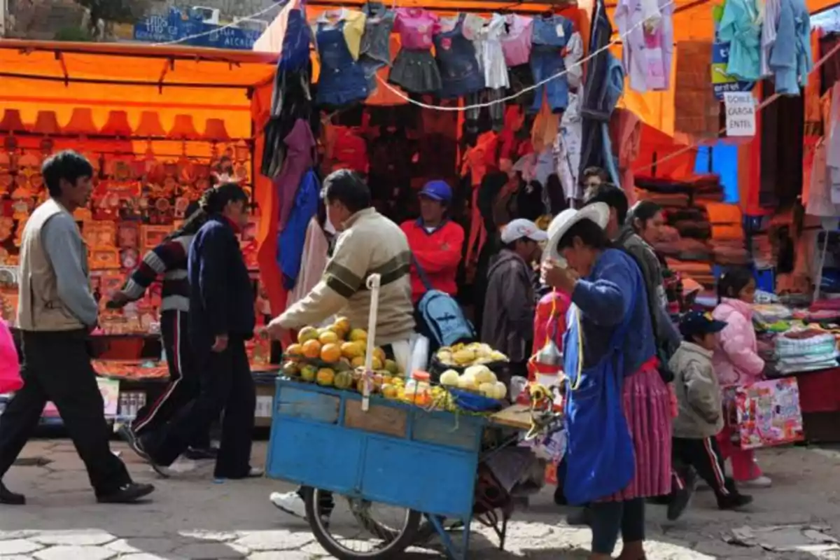 Personas caminando y comprando en un mercado al aire libre con puestos de ropa y frutas
