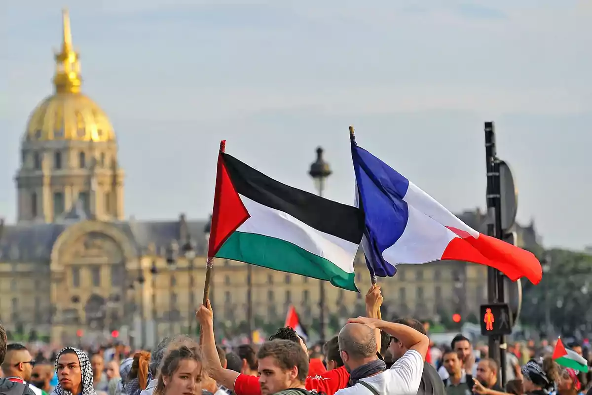 Personas en una manifestación sostienen las banderas de Palestina y Francia frente a un edificio histórico con cúpula dorada