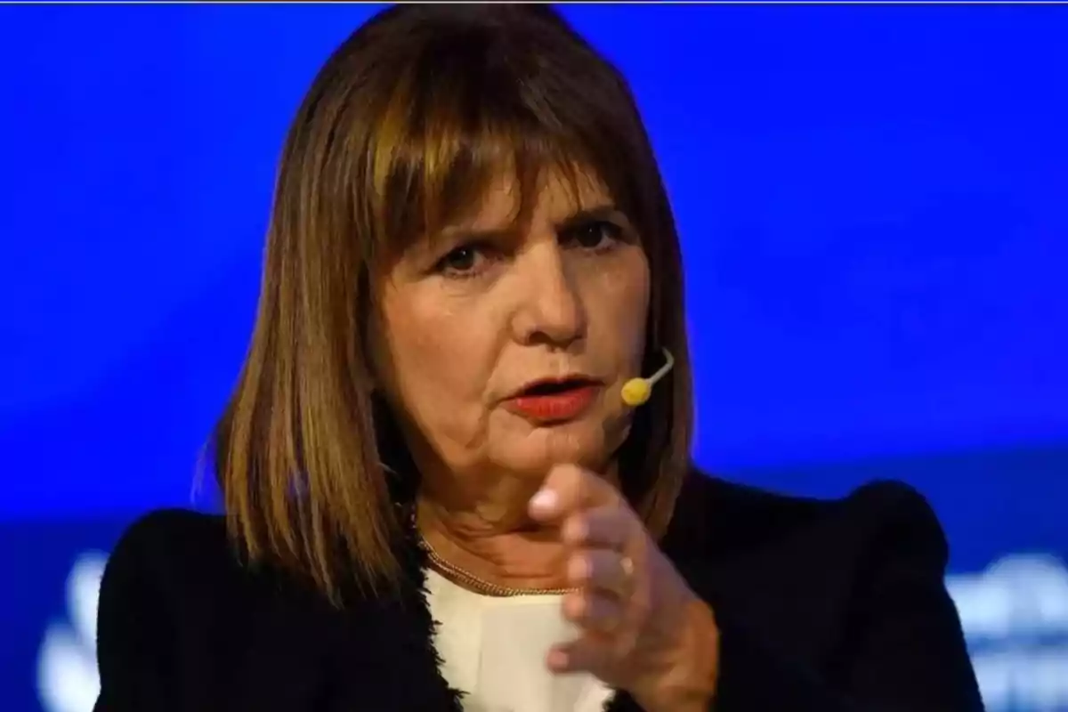 Brown-haired woman with straight hair wearing a headset microphone and speaking on a stage with a blue background Brown-haired woman with straight hair wearing a headset microphone and speaking on a stage with a blue background