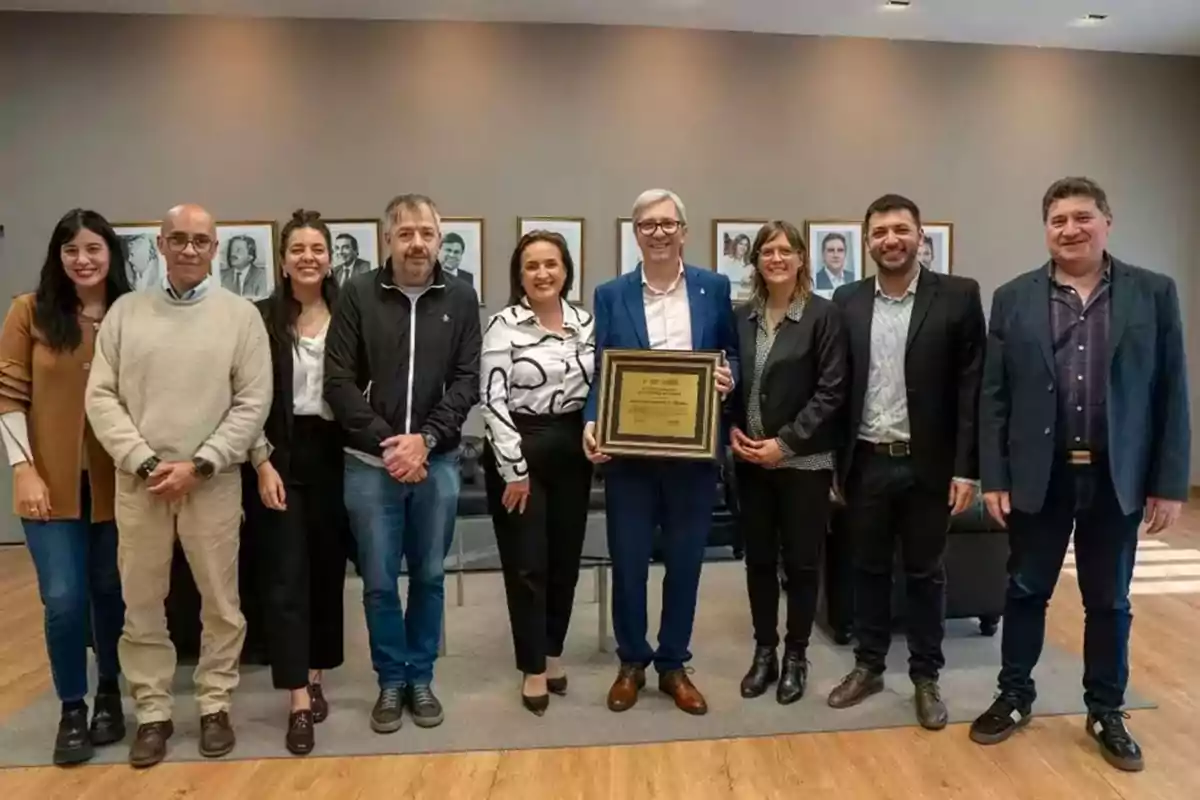 Group of nine people posing in an office while one of them holds a recognition plaque Group of nine people posing in an office while one of them holds a recognition plaque