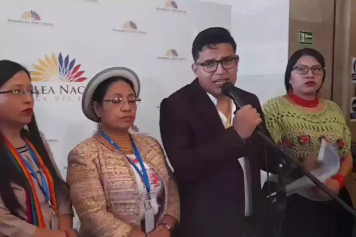 Cuatro personas indígenas están de pie frente a un micrófono en una rueda de prensa en un espacio institucional con un fondo que tiene el logo de la Asamblea Nacional de Ecuador Cuatro personas indígenas están de pie frente a un micrófono en una rueda de prensa en un espacio institucional con un fondo que tiene el logo de la Asamblea Nacional de Ecuador