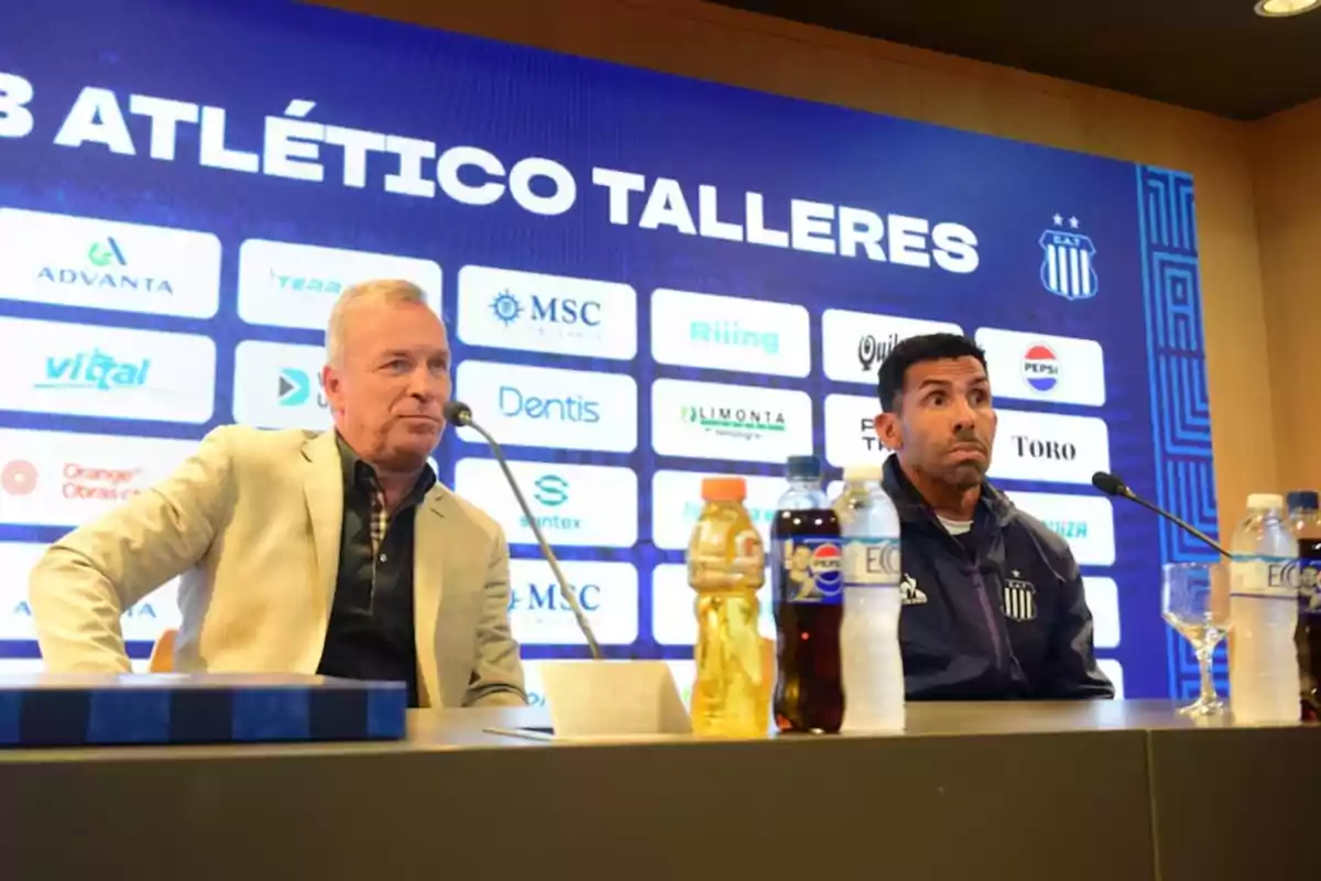 Two men sitting at a press conference of the Atlético Talleres club with several bottles of drinks on the table and a blue background with sponsor logos. Two men sitting at a press conference of the Atlético Talleres club with several bottles of drinks on the table and a blue background with sponsor logos.