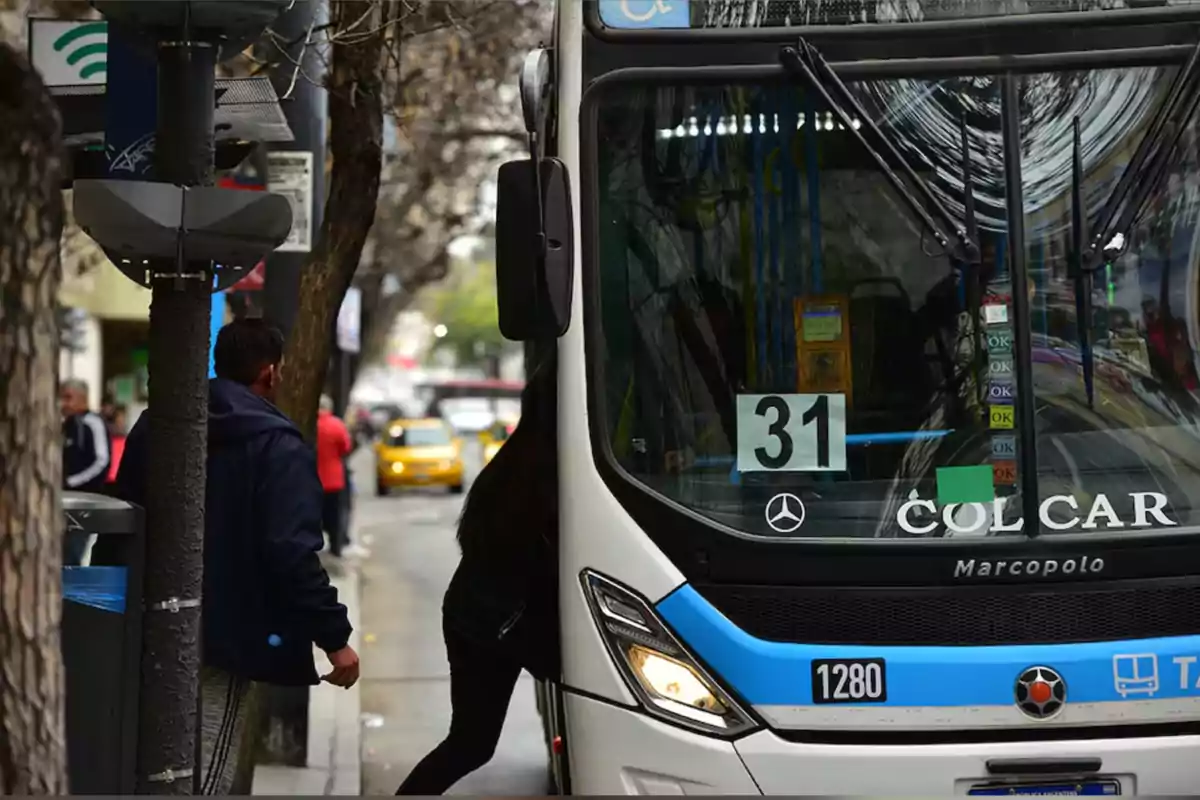 Persona subiendo a un colectivo urbano en una calle de ciudad con árboles y autos estacionados al fondo Persona subiendo a un colectivo urbano en una calle de ciudad con árboles y autos estacionados al fondo