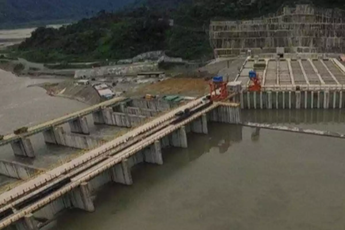 Vista aérea de una represa hidroeléctrica en construcción rodeada de montañas y vegetación