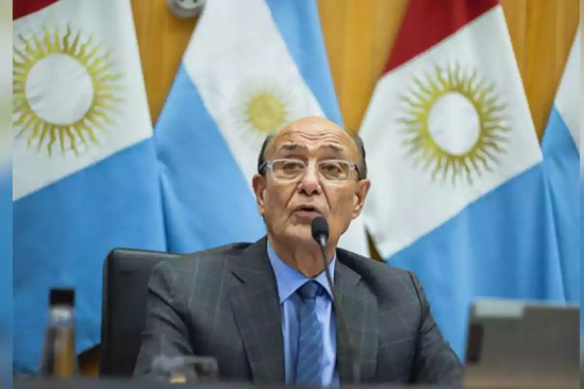 Hombre mayor con gafas hablando frente a un micrófono con banderas de Argentina de fondo Hombre mayor con gafas hablando frente a un micrófono con banderas de Argentina de fondo