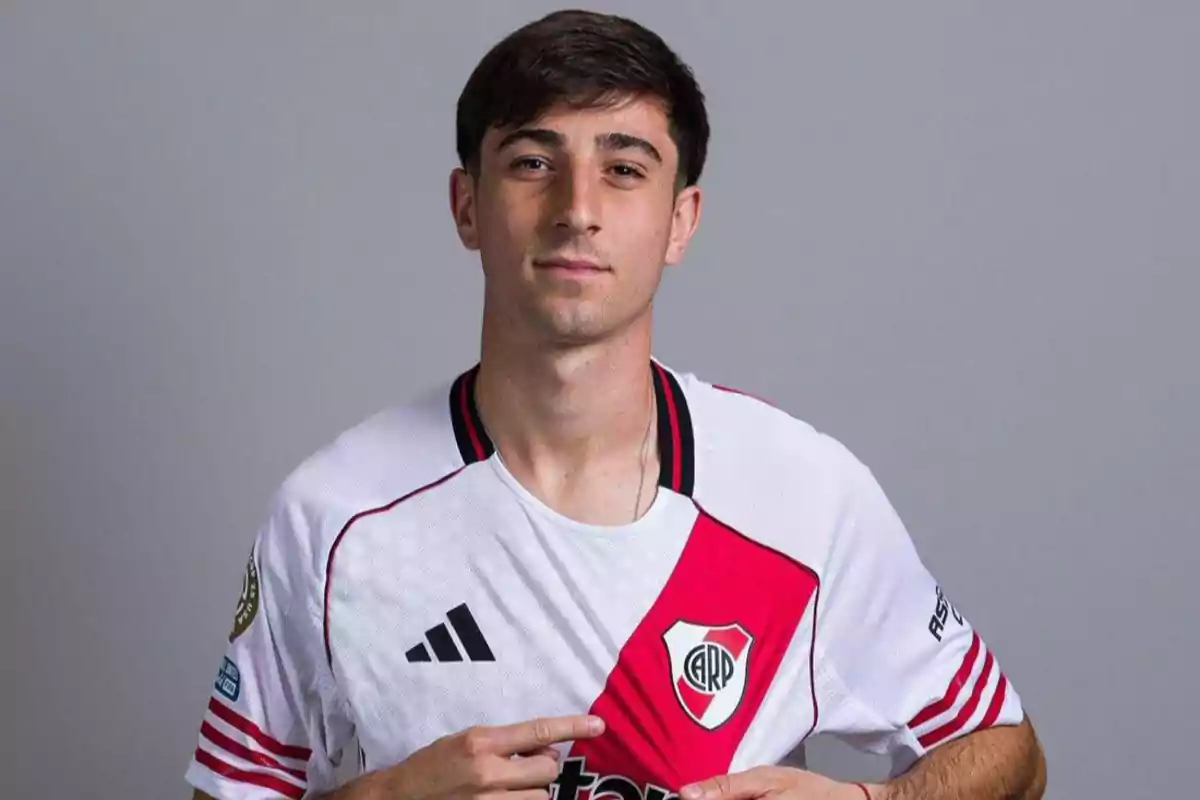 Young man wearing a River Plate jersey pointing to the team’s crest against a gray background Young man wearing a River Plate jersey pointing to the team’s crest against a gray background