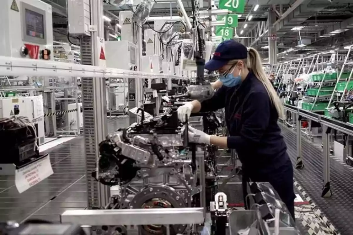 Trabajadora con mascarilla y guantes ensamblando un motor en una línea de producción industrial moderna Trabajadora con mascarilla y guantes ensamblando un motor en una línea de producción industrial moderna